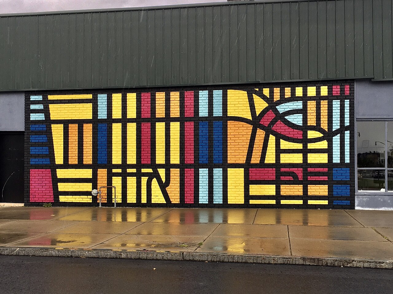 As seen on a rainy afternoon in May 2021, the mural on the Commonwealth Avenue side of the building at 1256 Hertel Avenue in the North Park section of Buffalo, New York is entitled We Are Here. It was