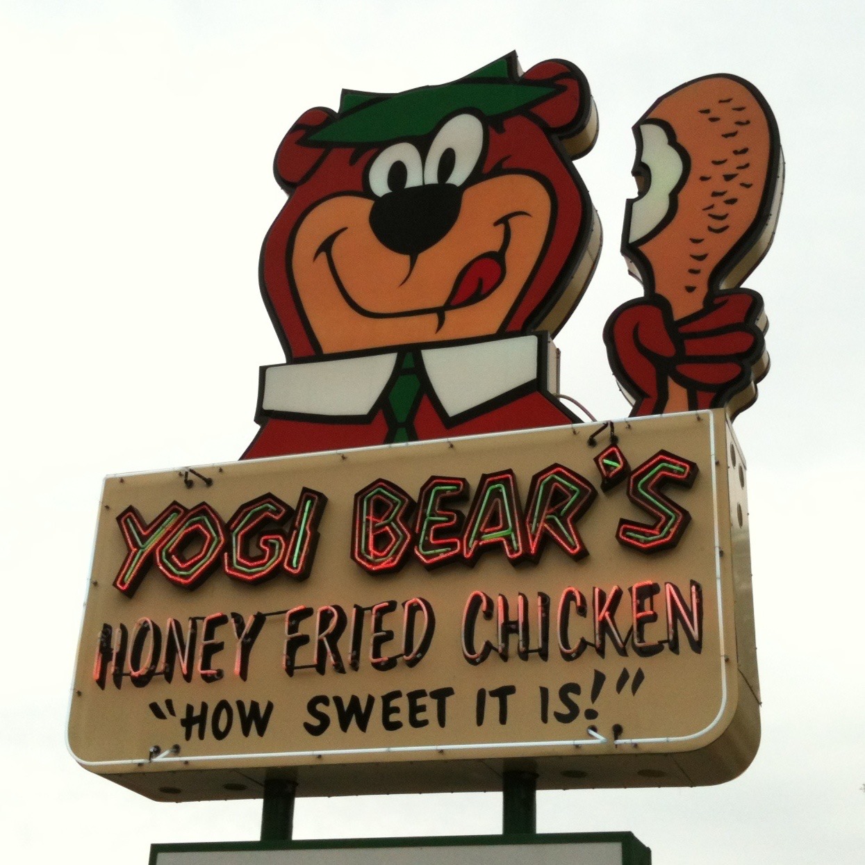 Sign of Yogi Bear's Honey Fried Chicken with Yogi Bear holding a chicken drumstick and the catchphrase "How sweet it is!"