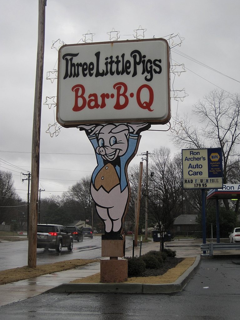 The building at Three Little Pigs Bar-B-Q, Memphis, with the roofline pigs and a catering trailer carrying the same three pigs on its side.