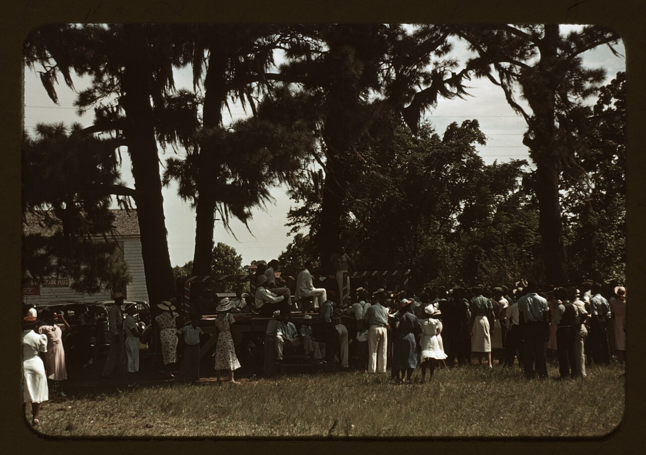 Colour transparency, 1939: a crowd under pines hung with Spanish moss at a Fourth of July celebration on St. Helena Island, South Carolina, with washtubs and cooking pots on the ground.
