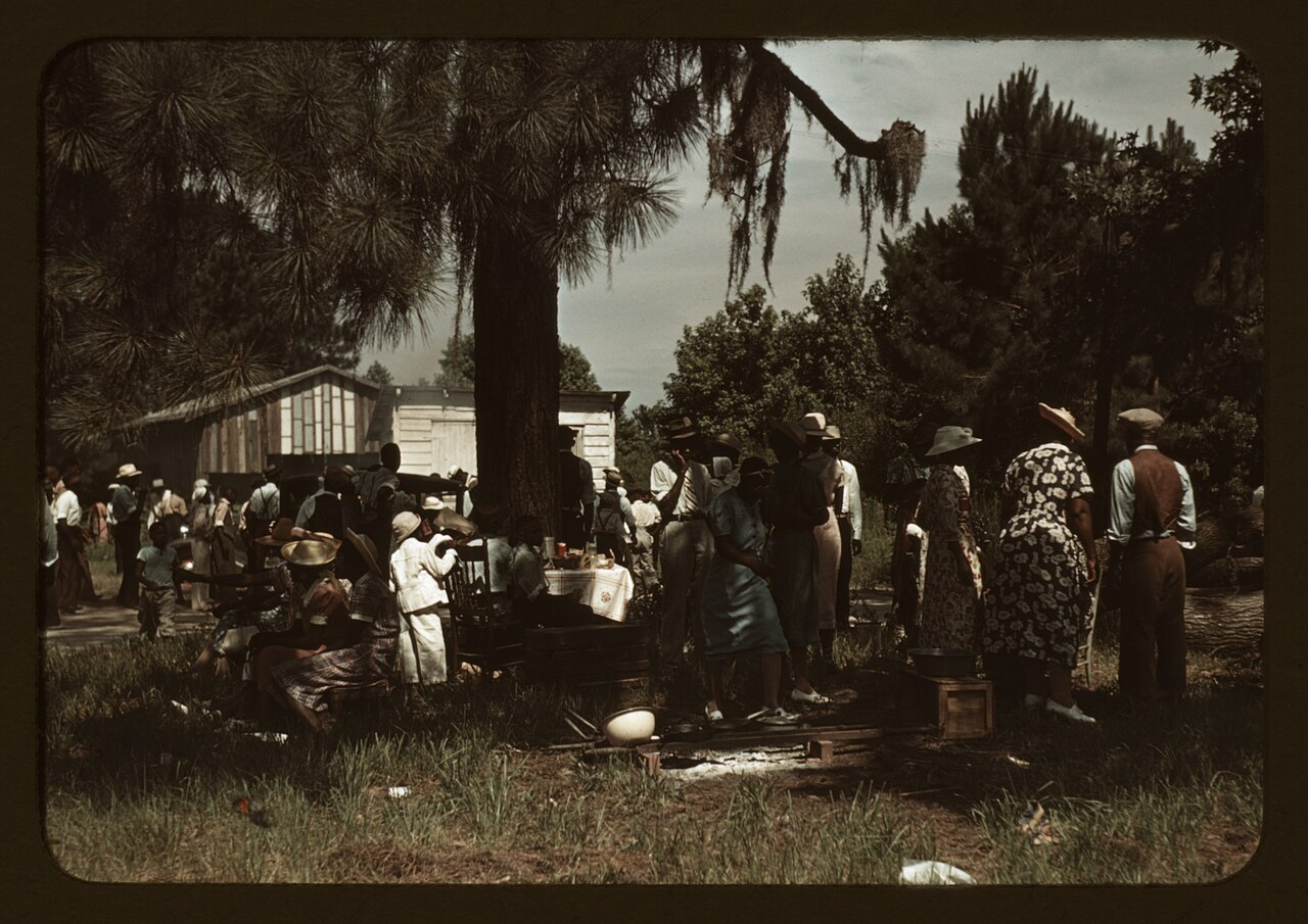 Colour transparency, 1939: a cloth-covered table under the pines at the Fourth of July picnic on St. Helena Island, South Carolina, with tubs, crates and a pot set out around it.