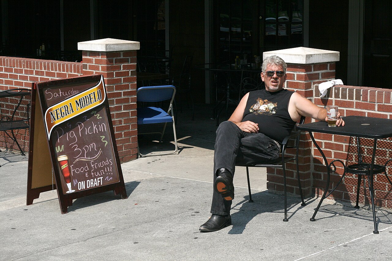 A patron waits outside with a beer at Charlie's Pub &amp; Grille on Ninth Street in Durham, North Carolina.  The advertised pig pickin' is about to commence.
