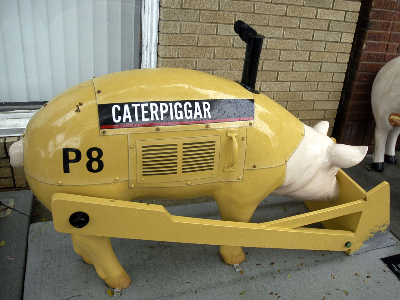 Caterpiggar: a pig sculpture painted as a yellow Caterpillar bulldozer, with an exhaust stack, a radiator grille, a dozer blade across the front, P8 on the flank and CATERPIGGAR lettered in the machine-maker's typeface.