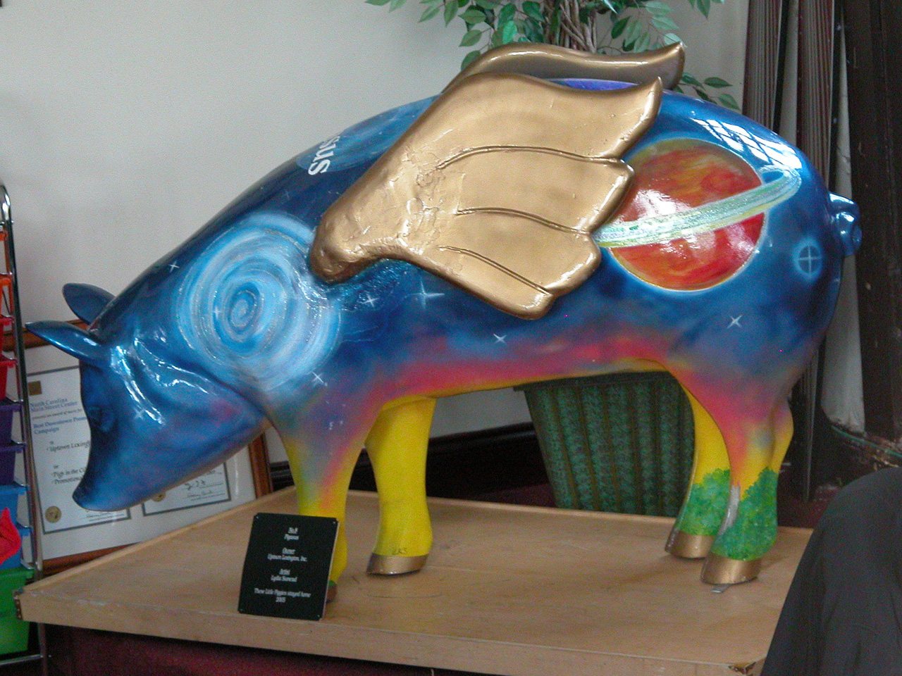 Pigasus: a deep blue pig sculpture with gold wings, planets and stars painted over it and yellow and green trotters.