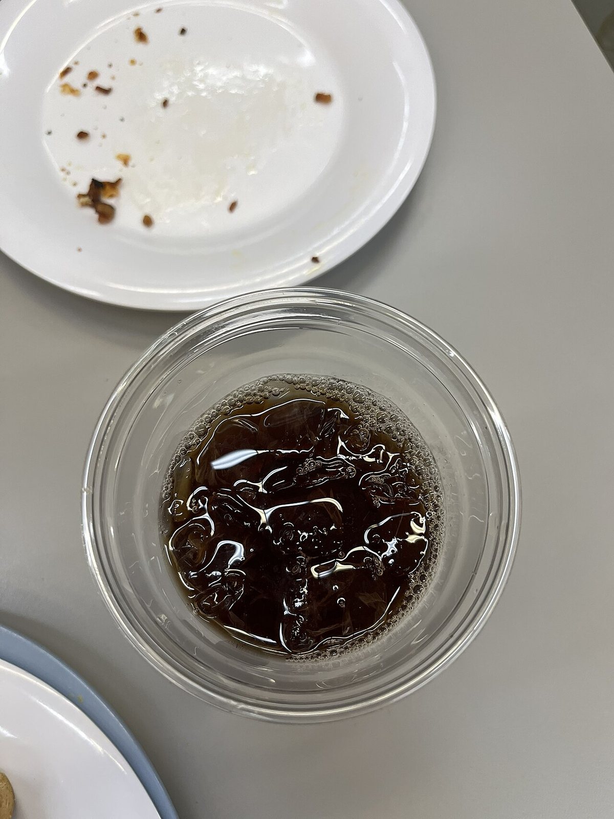 Glass of sweet tea from The Grill at Ole Miss in a clear plastic cup, on a grey table with a dirty white plate in the background.
