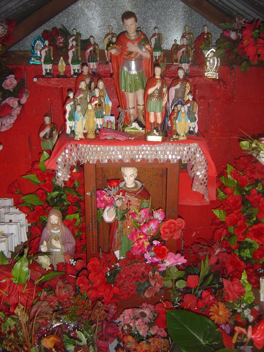 Red altar crowded with Saint Expedite statues, flowers and candles, Réunion.