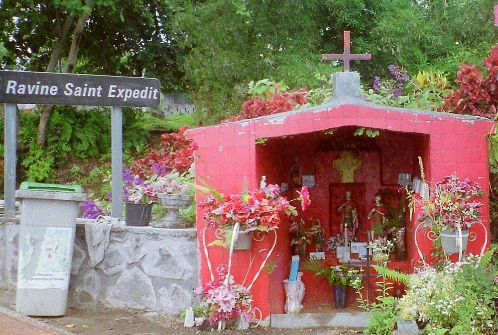 Red chapel of Saint Expedite beside a road sign reading Ravine Saint Expedit, Réunion.