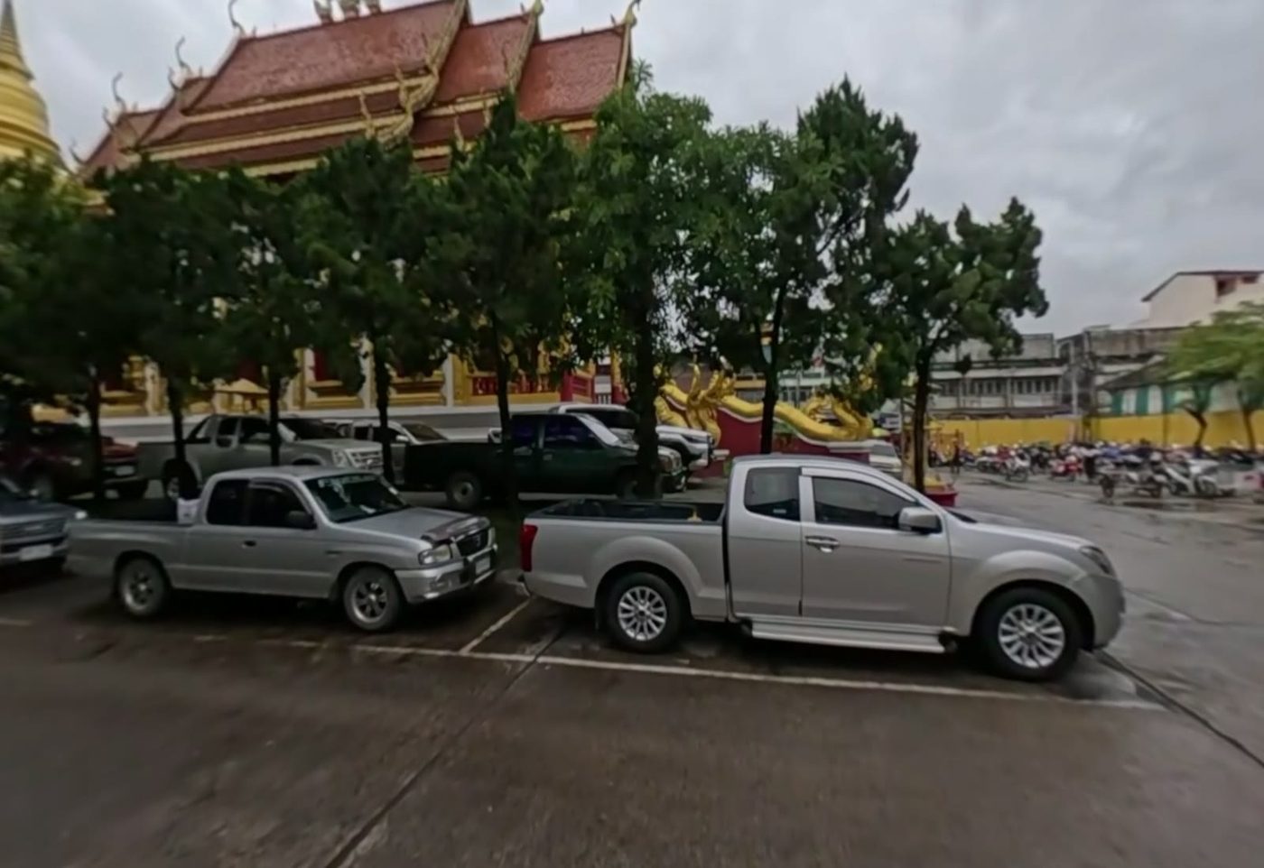 Red-roofed temple hall, golden chedi and naga behind the car park trees