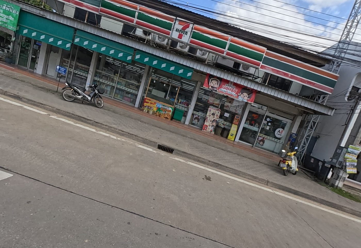 7-Eleven shop in a row of shophouses on a suburban road, with motorbikes parked outside