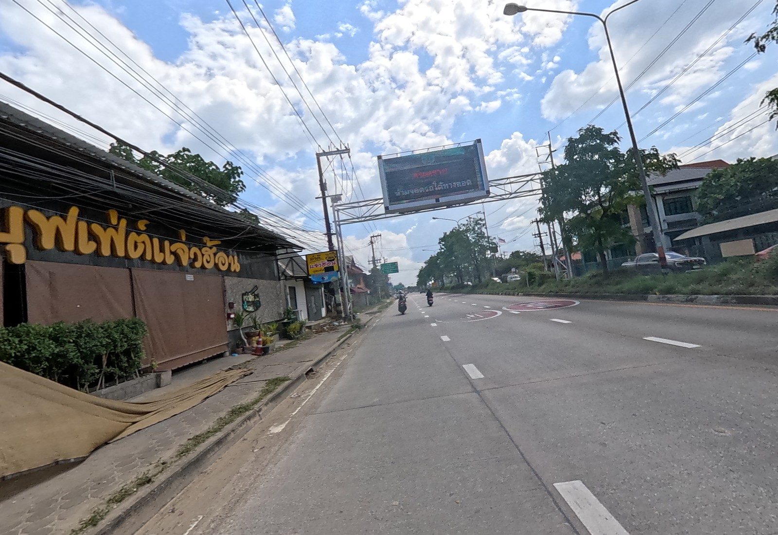 The highway ahead past the restaurant sign บุฟเฟ่ต์แจ่วฮ้อน and a yellow แจ่วฮ้อน standing sign, under an LED gantry sign.