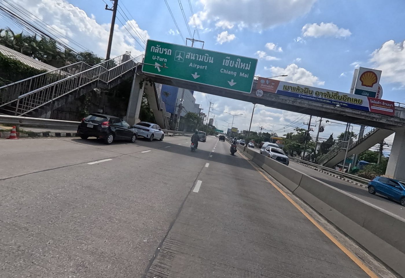 Airport and Chiang Mai direction sign on a footbridge over the highway, with a Shell station beside it