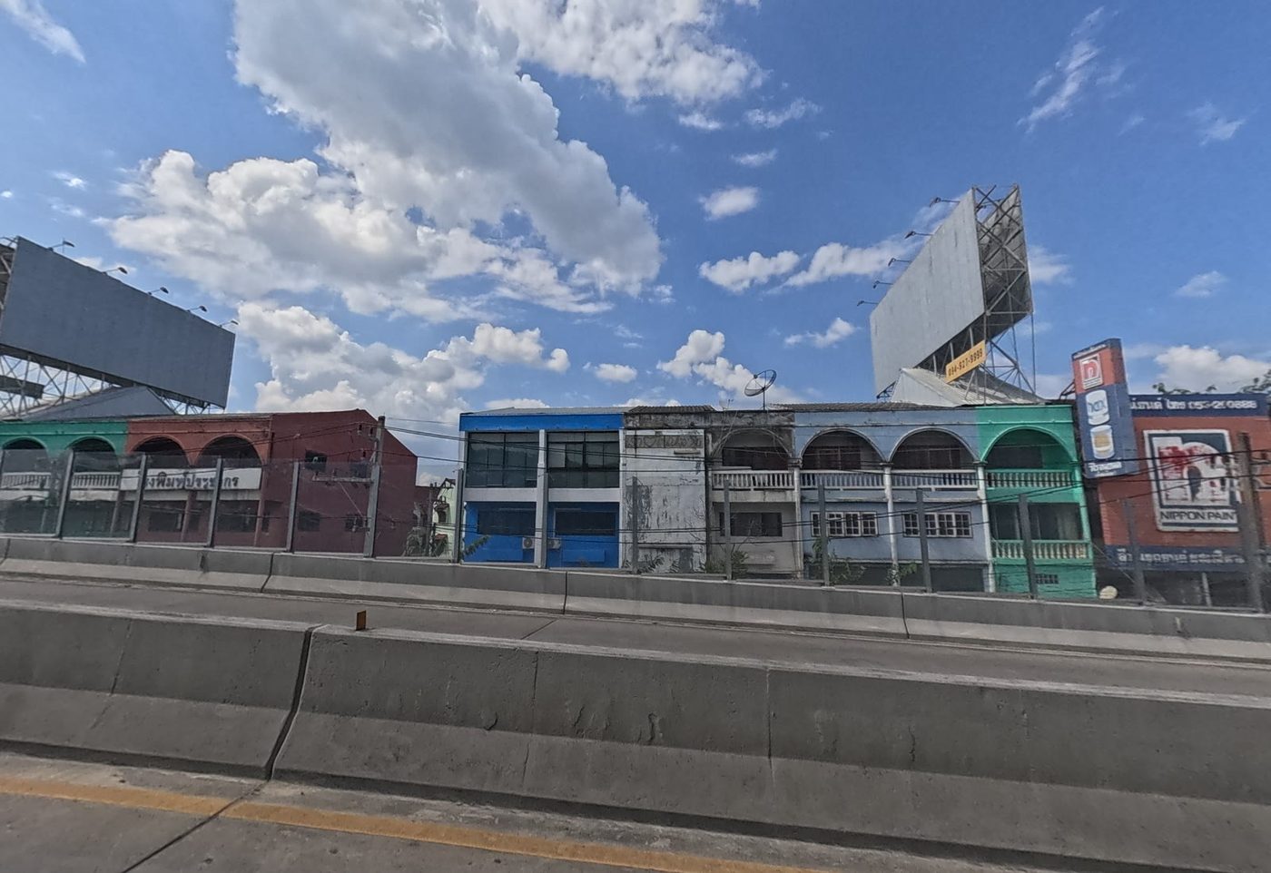 Row of colourful old arched shophouses along the highway, with a Nippon Paint shop at the end