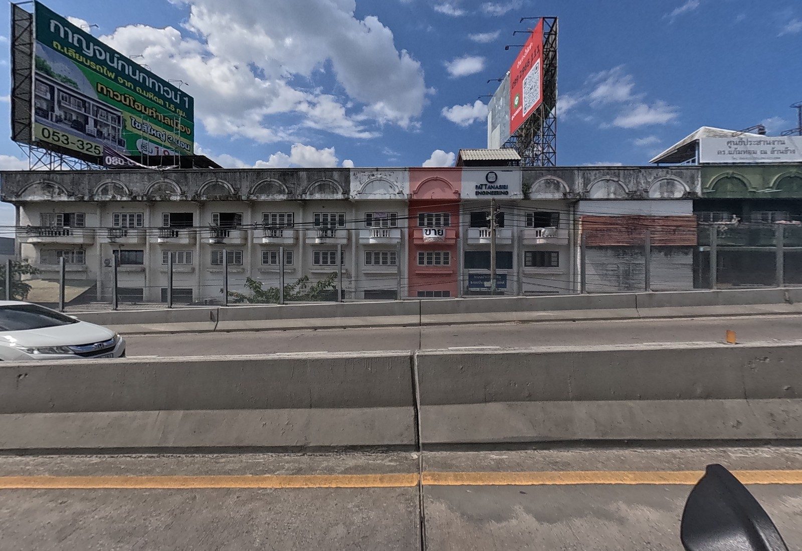 Across the flyover, a long row of old three-storey shophouses: an engineering firm, a pink unit for sale, and rooftop billboards.