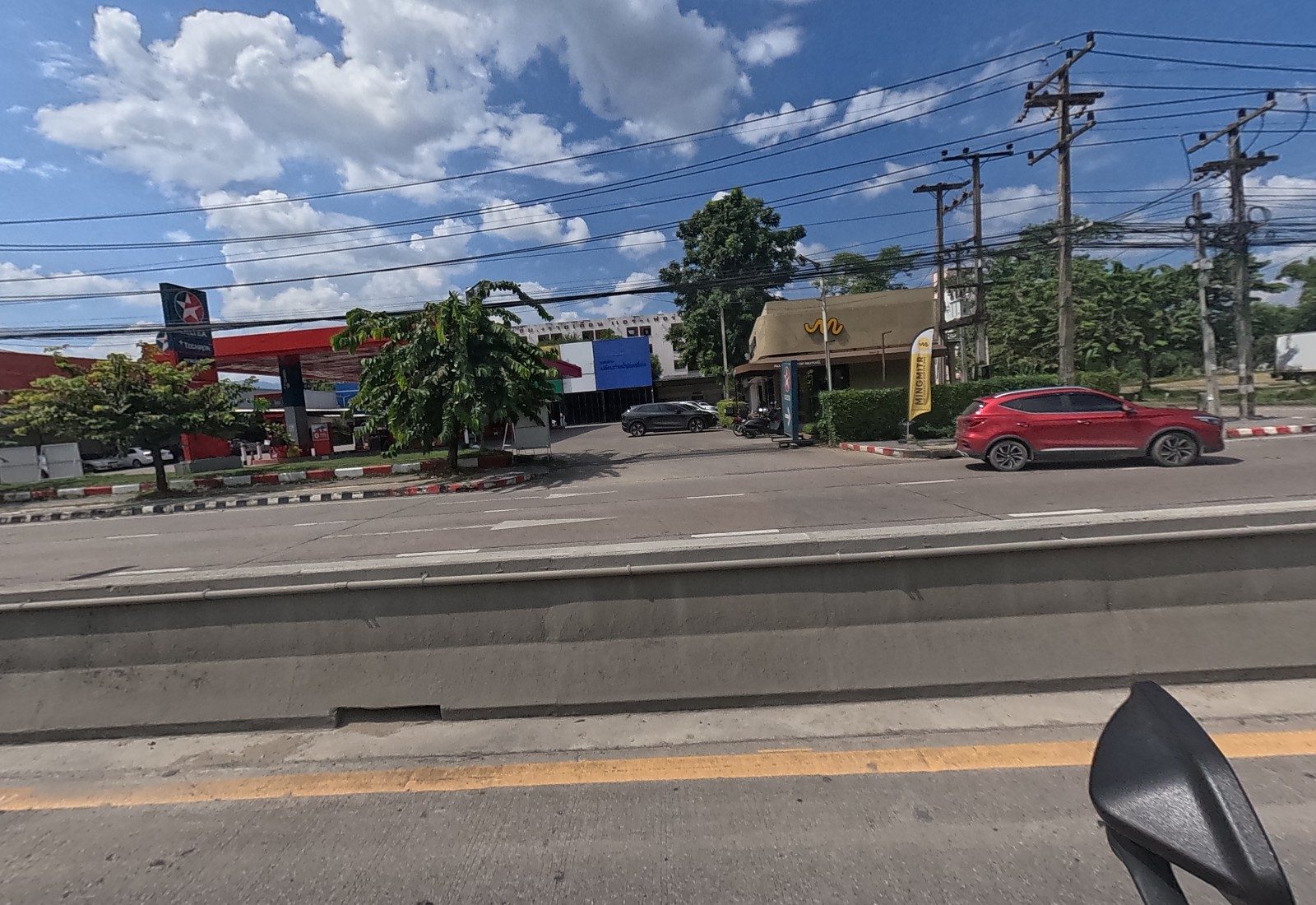Across the road, a Caltex petrol station, a blue-signed shop behind it, and a MINGMITR coffee shop with a yellow logo and flag; a red SUV passing.