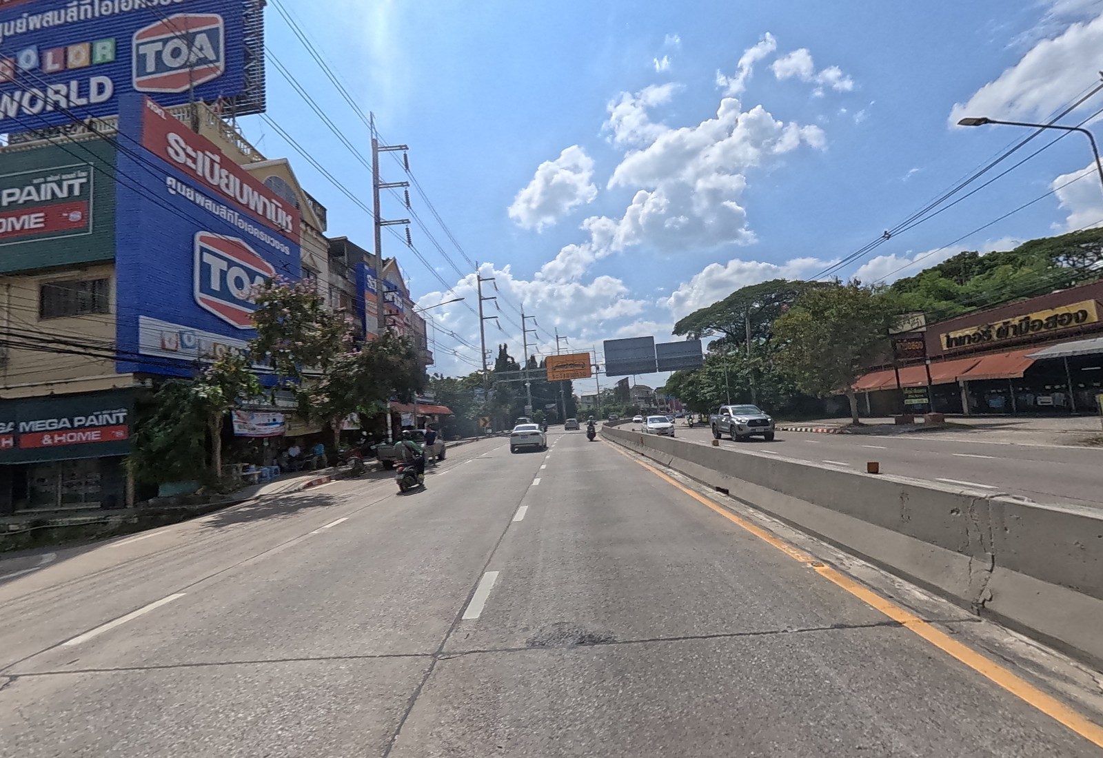 Mahidol Road ahead: the big ระเบียบพานิช TOA building on the left, a second-hand clothes market on the right, an overhead sign gantry ahead.