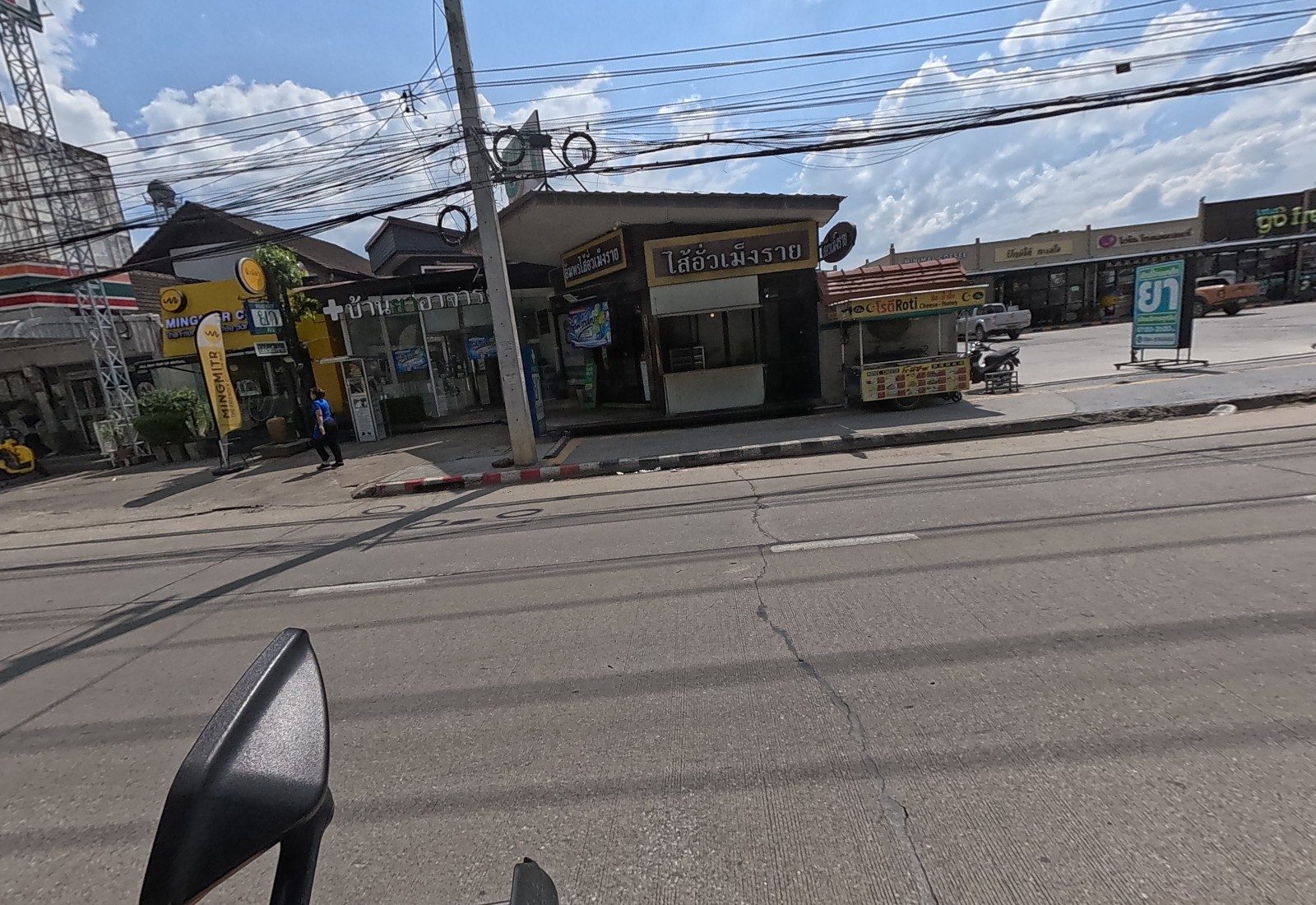 A row of small shops: Mingmitr coffee, a pharmacy, a Meng Rai sai ua sausage shop and a roti cart, with the Lotus's go fresh plaza beyond.