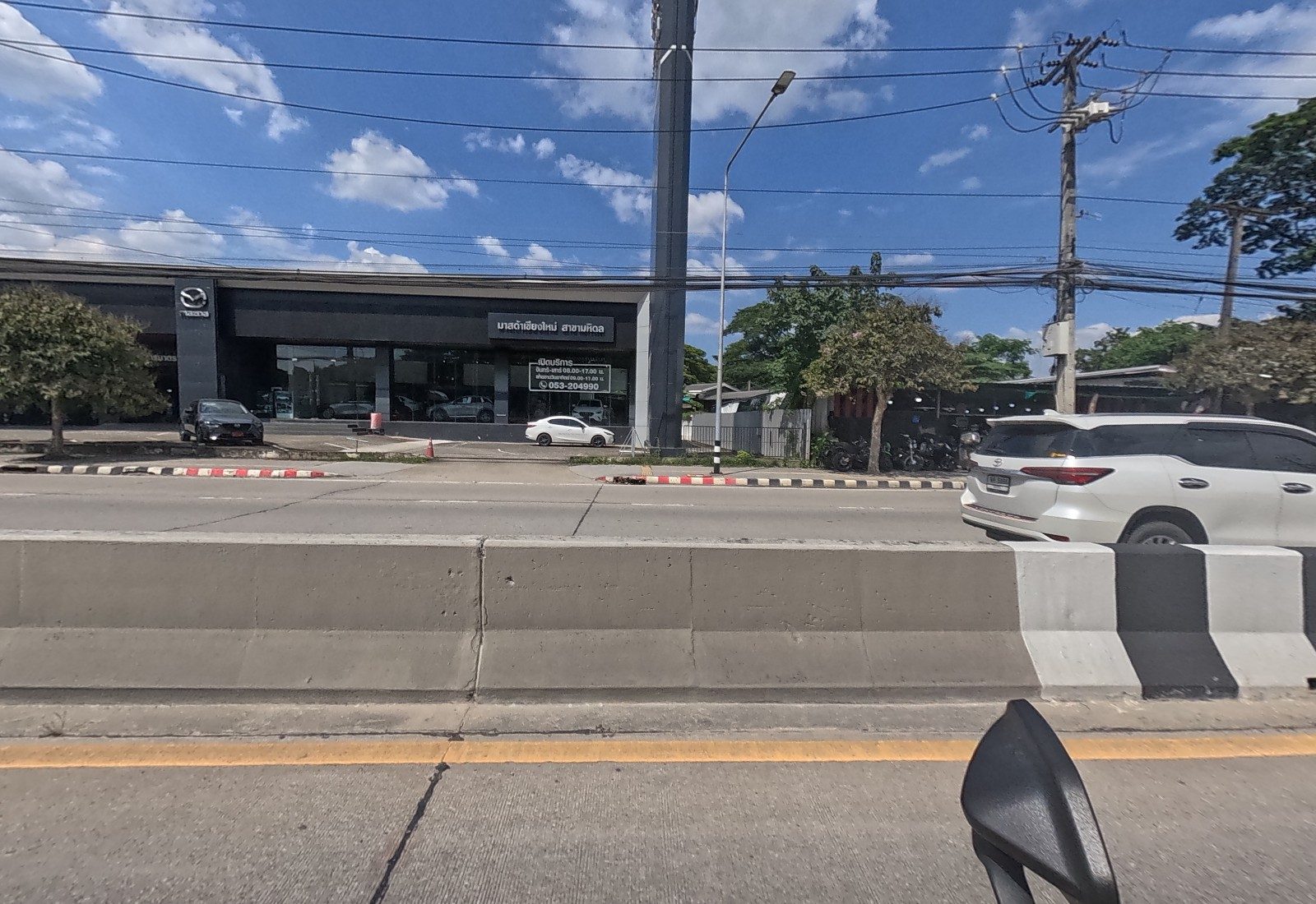Across the median stands the dark Mazda Chiang Mai Mahidol showroom with its hours posted on the glass.