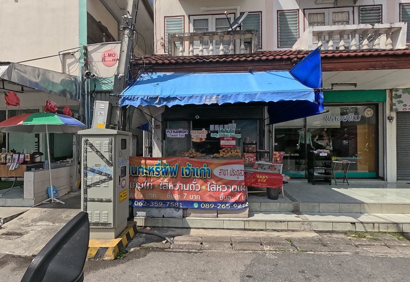 A curry-puff stall under a blue awning with trays of puffs and a big price banner, a painted utility cabinet, a clothing shop and a drinks stand beside it.
