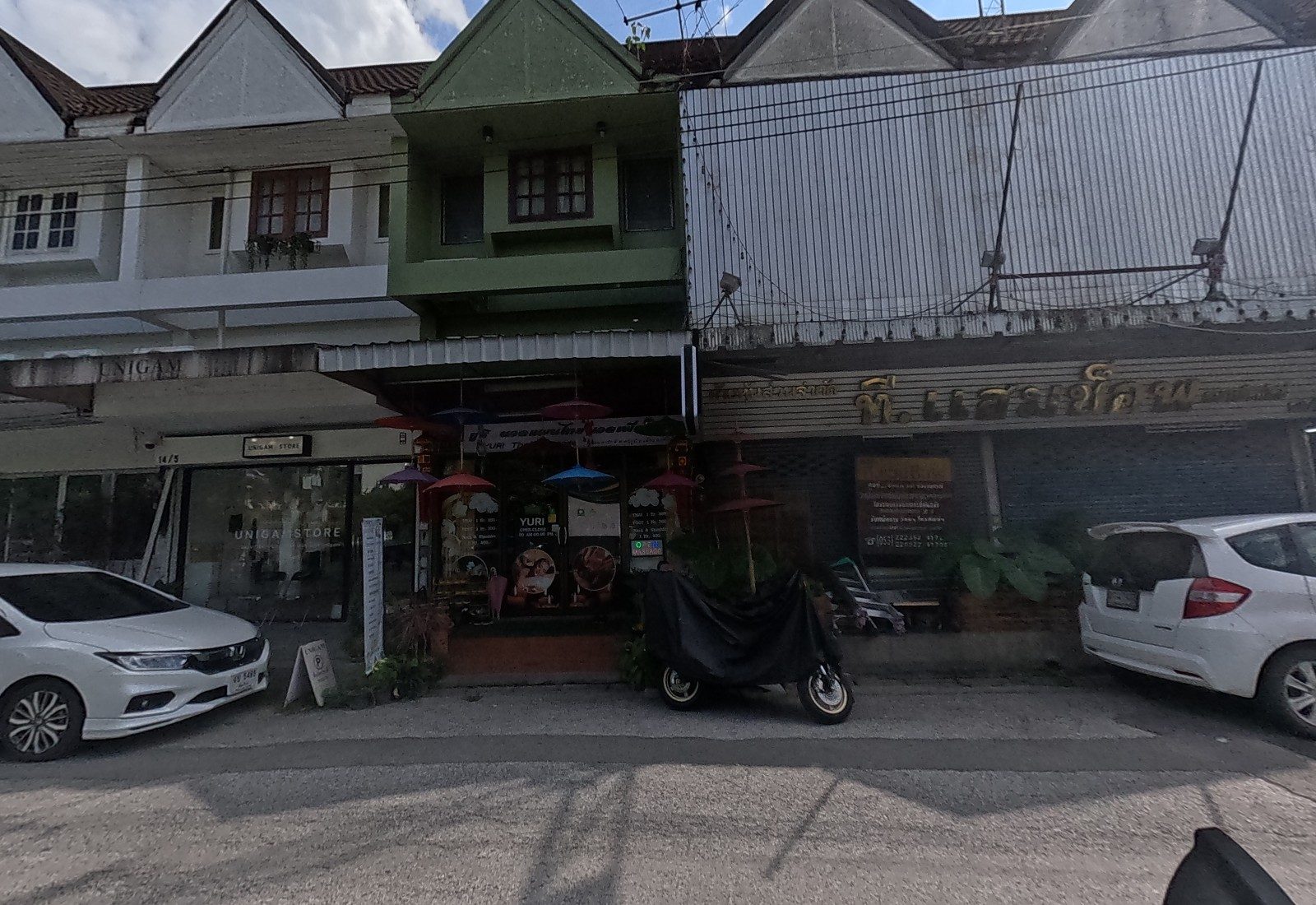 UNIGAM STORE, the green shophouse of Yuri Thai Massage hung with paper umbrellas, and the shuttered T.Ham Shop with a price board.