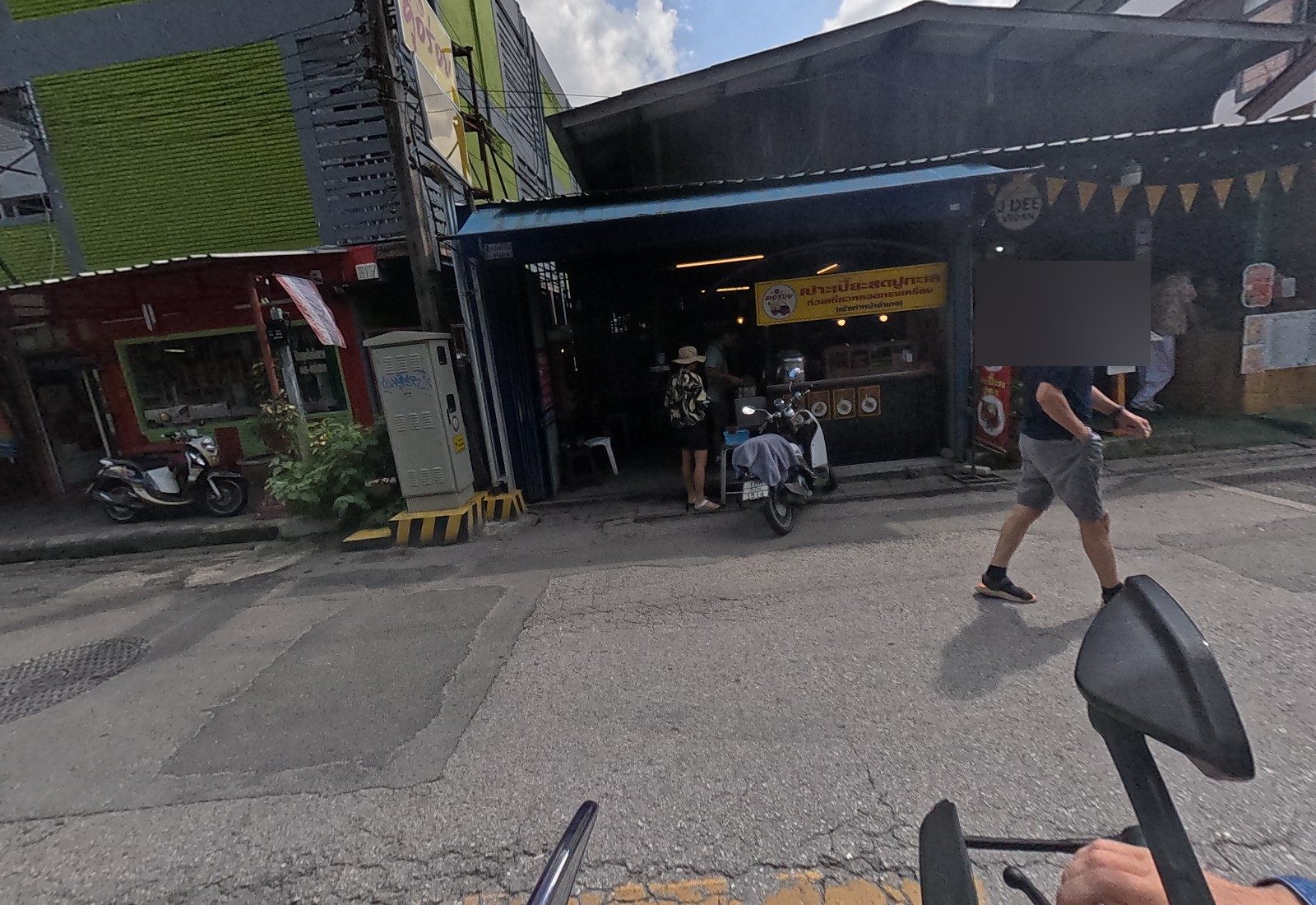 คู่อร่อย's open shopfront under a blue awning advertises fresh crab spring rolls and stuffed rice-noodle rolls, next to the J DEE Vegan restaurant; a man walks past.