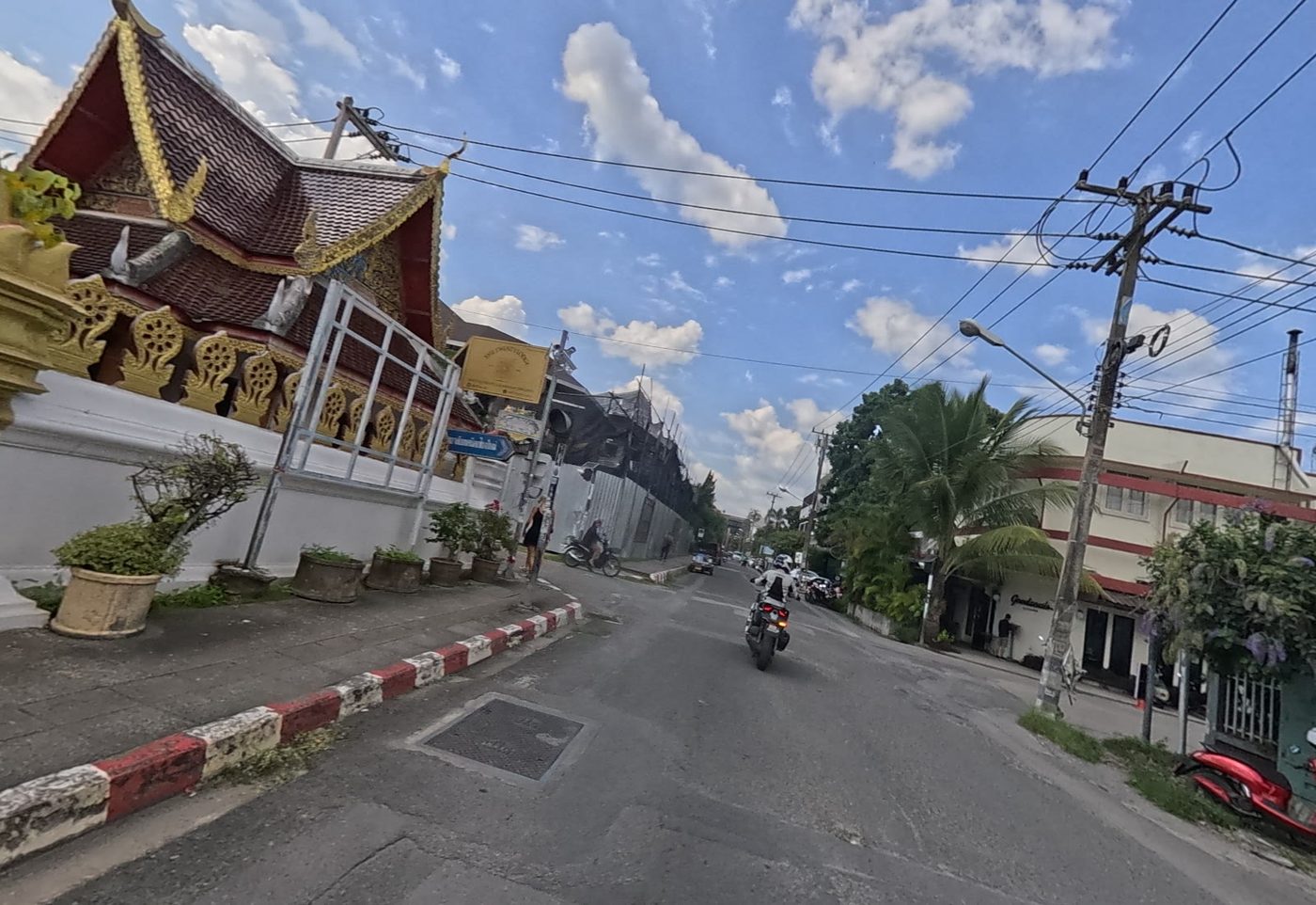 Street with an ornate Lanna wat gate and roof on the left