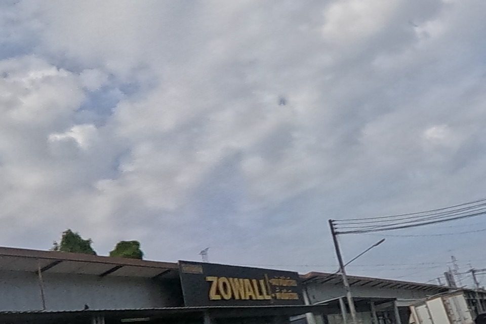 The road runs past a shophouse row to a ZOWALL-branded shop and a yellow apartment building further on.