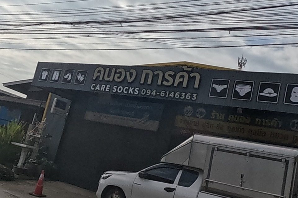 A trading shop named Khanong Karnka sells socks and clothing under a Care Socks sign, a food cart parked beside it.