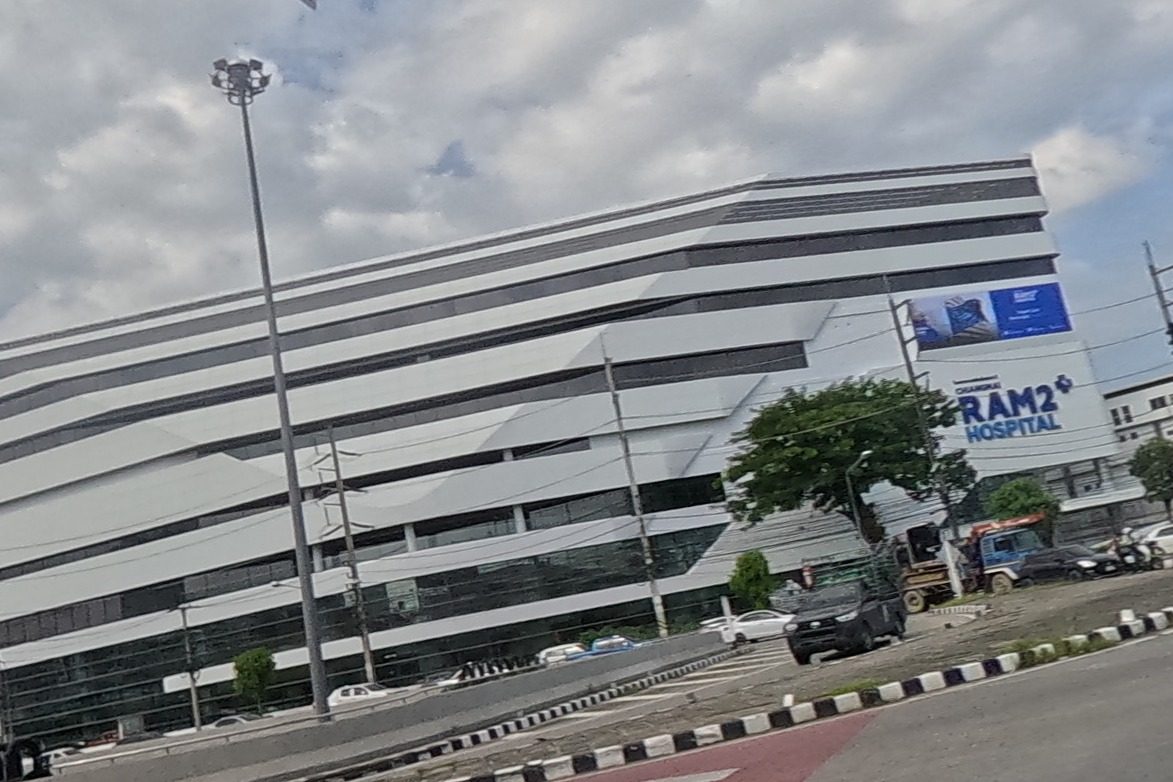 A large striped modern building signed RAM2 Hospital stands at the junction, with traffic waiting at a red light.