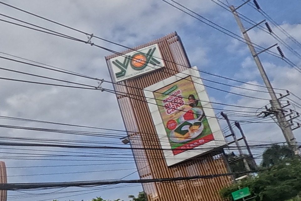 The YOK tower sign is seen close-up with an orange sunburst logo and a poster advertising a rice-cake dessert; traffic cones and a green taxi-stand sign stand nearby.