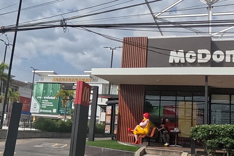 McDonald's frontage includes a Ronald McDonald statue seated on a bench, near a 7-Eleven.