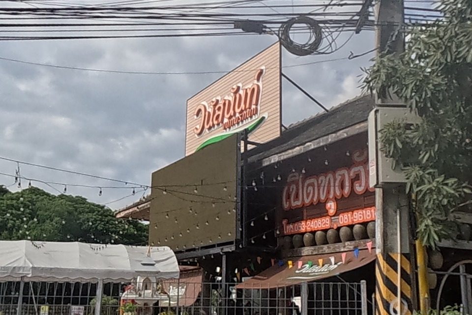 A garden restaurant called 'Vanusnun' with a pink cursive sign, string lights, outdoor tables, and a small white statue on a pedestal at the entrance.