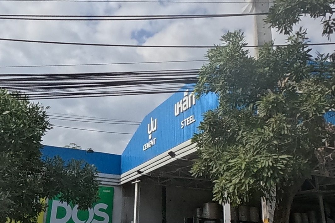 A large blue building-materials store selling cement and steel, with brand boards for Hafele, DOS Life paint, and Tokay Gecko brand cement.