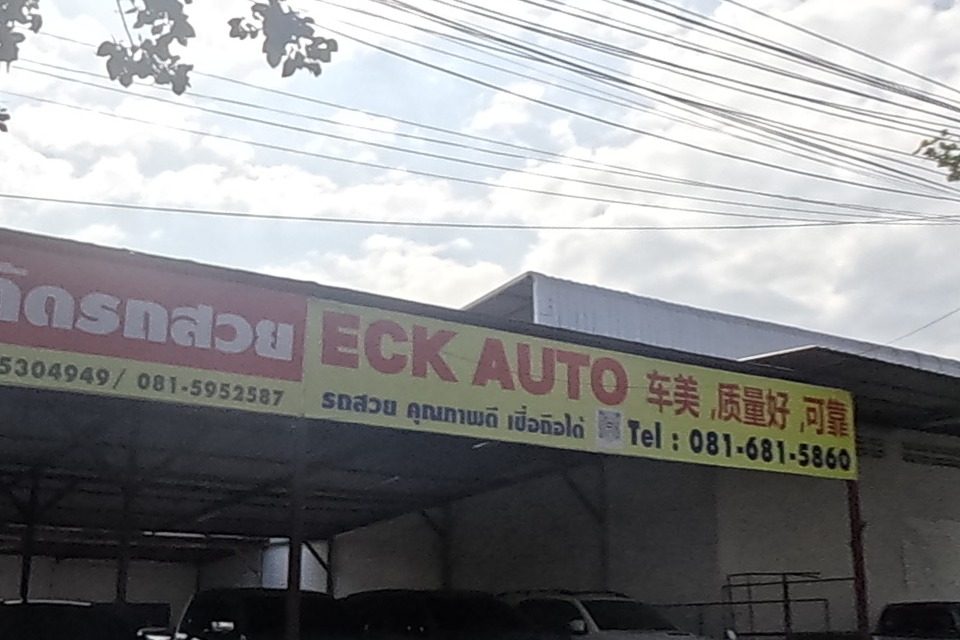 ECK AUTO's used-car lot on the left with a clear sign and phone number; the road continues straight with light traffic.