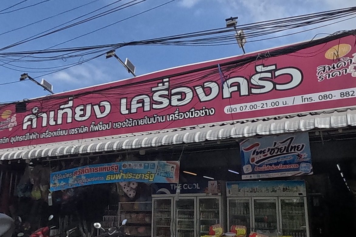 A hardware and kitchenware shop 'คำเที่ยง เครื่องครัว' (open 07.00-21.00, tel 080-882-4149) displays fridges of drinks and a table of snacks, with a beverage warehouse of stacked Chang, Leo and Heineken crates next door.
