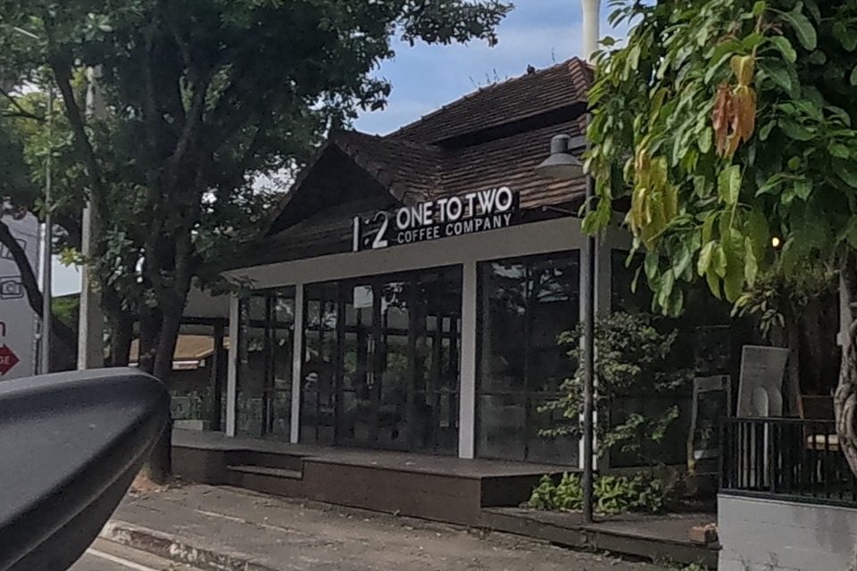 '1:2 ONE TO TWO COFFEE COMPANY' occupies a glass-fronted teak-roofed corner building, next to 'Somtum House - Yokkrok' (Thai salad / healthy Thai food) behind a large tree with exposed roots.
