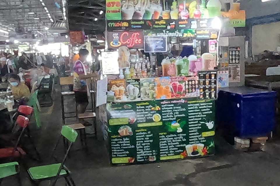 The main hall of the market building: dealers at tables of amulets, a table of brass footed bowls and an open book of drawings, drinks stall 678 on the right.
