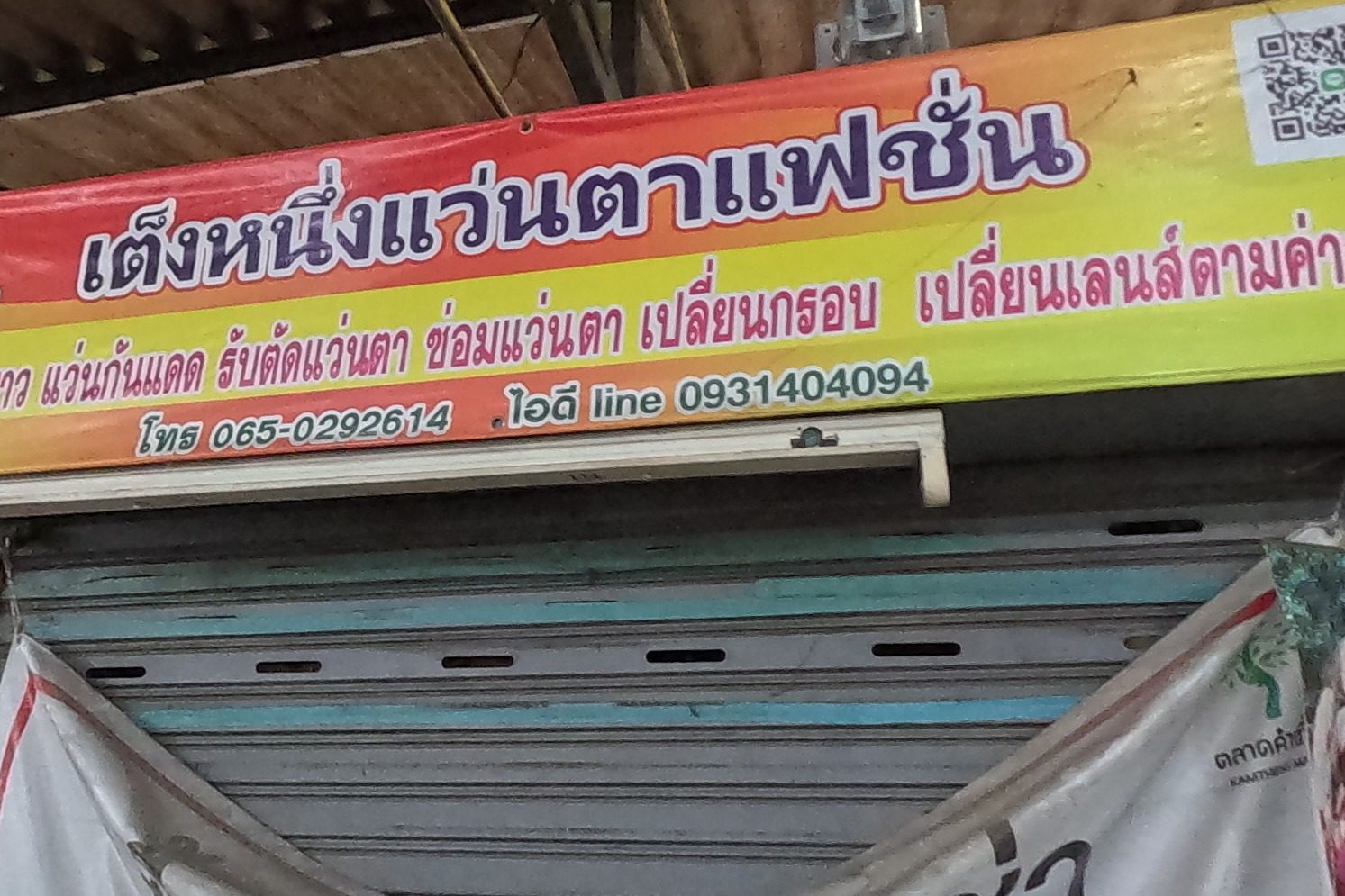 The optician's shuttered front under its bright sign, the market office's 'space for rent' banner and a monk's New Year poster.