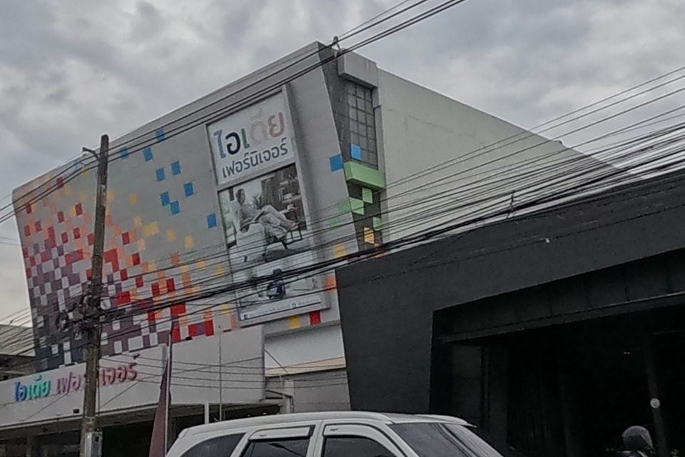 Idea Furniture store in a dark angular building with a colourful pixel-art mural on its side wall, cars passing on the road.