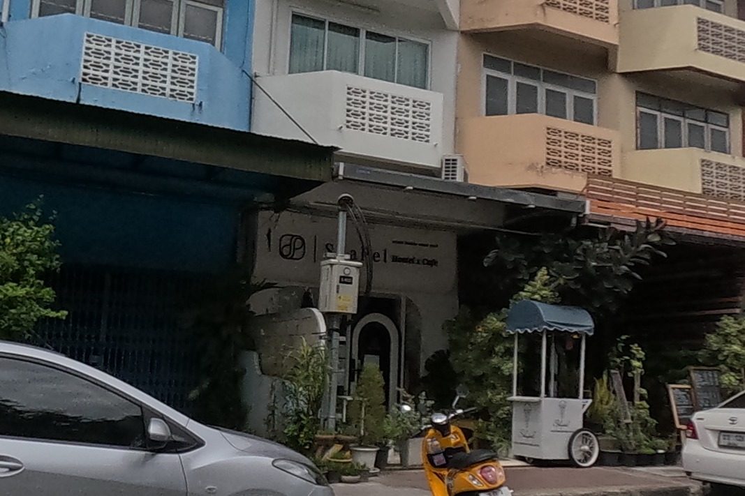 A row of shophouses with brown, blue and cream balconies, a hostel-cafe sign on one storefront.