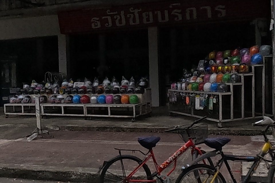 A motorcycle helmet shop with racks of helmets, next to a food stall under a GrabFood umbrella.