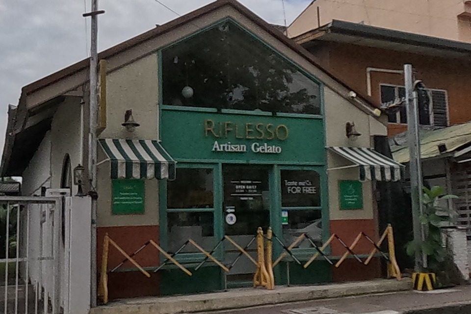 An artisan gelato shop with a green gabled front, folding security gates open for the day.