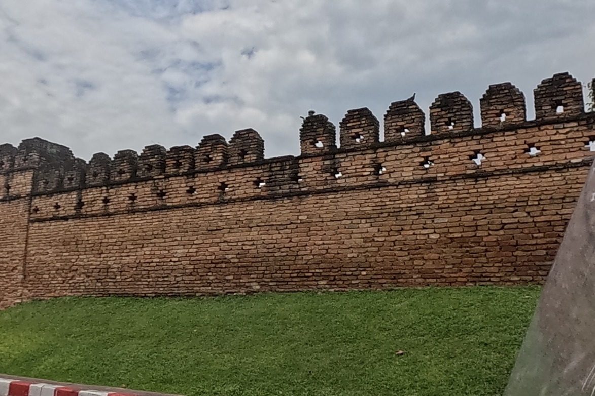 A crenellated brick city wall with a fresh lawn in front sits at a corner of the old moat.