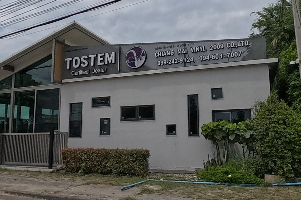 A grey building with a TOSTEM certified-dealer sign shared with Chiang Mai Vinyl 2009 Co., Ltd, phone numbers posted.