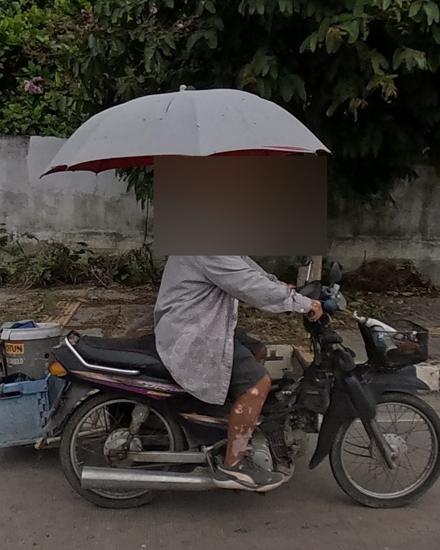 A motorbike vendor rides under a rigged umbrella