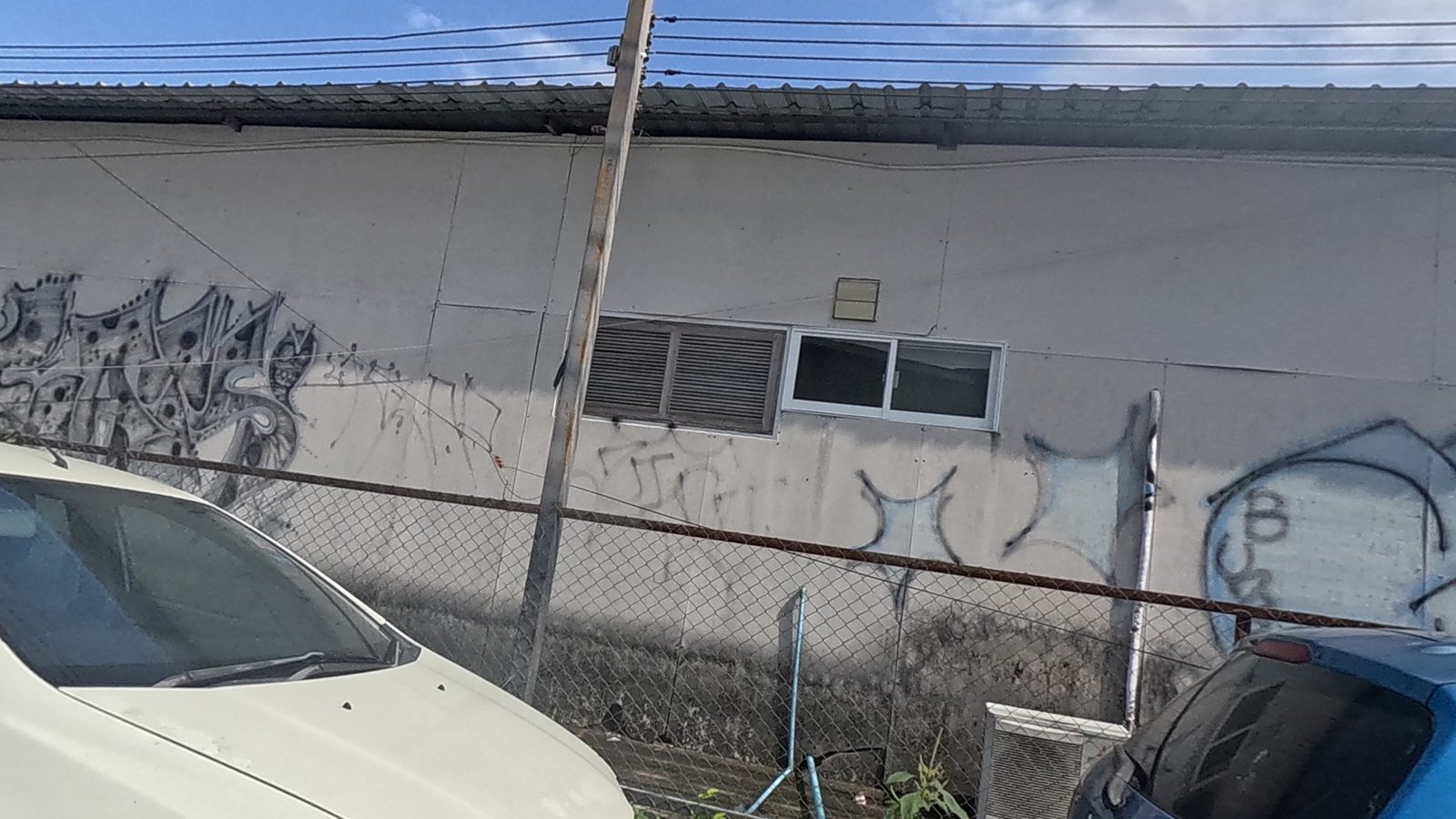 Silver tag row on a warehouse wall behind a chain-link fence
