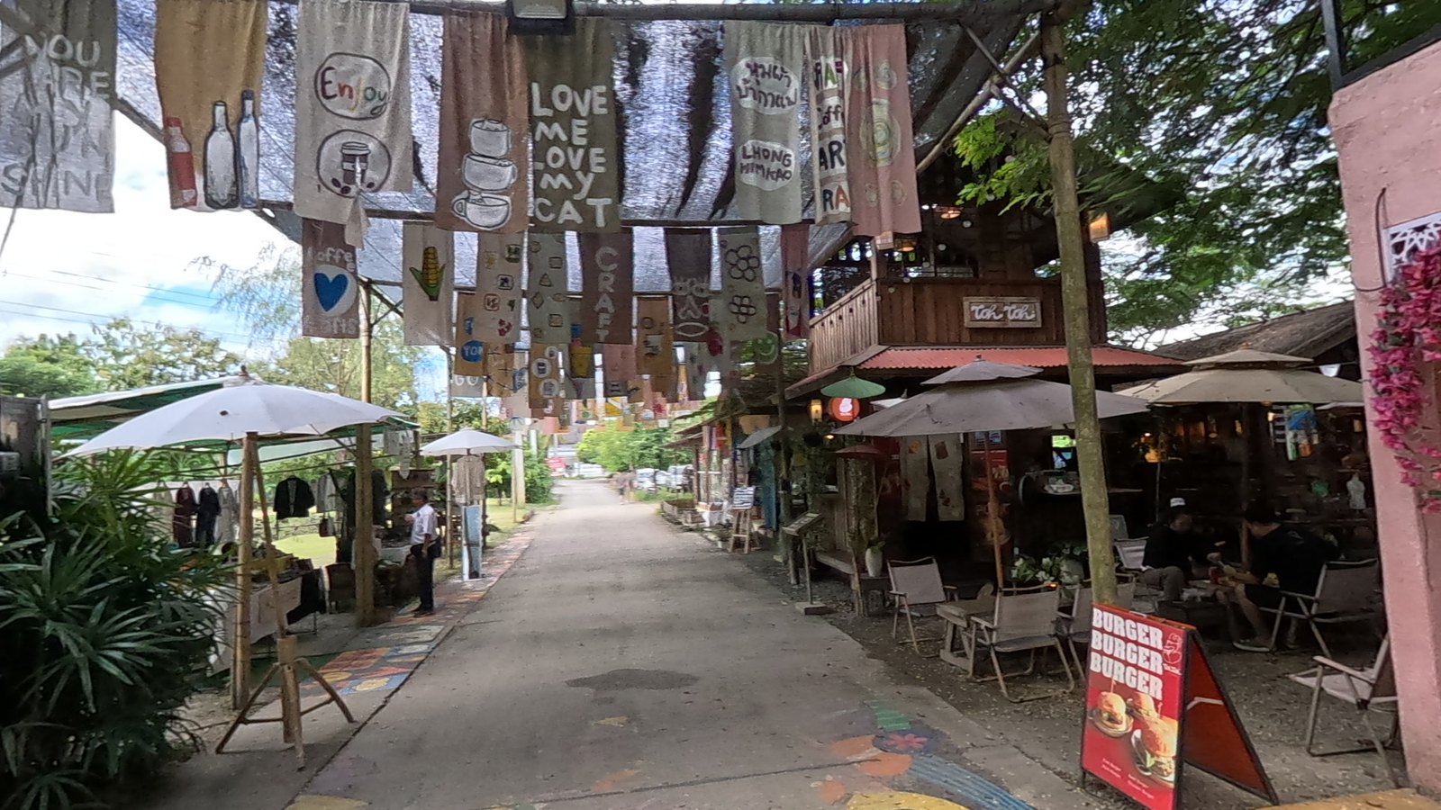 Painted banners and flowers on the path — Chamcha Market, San Kamphaeng