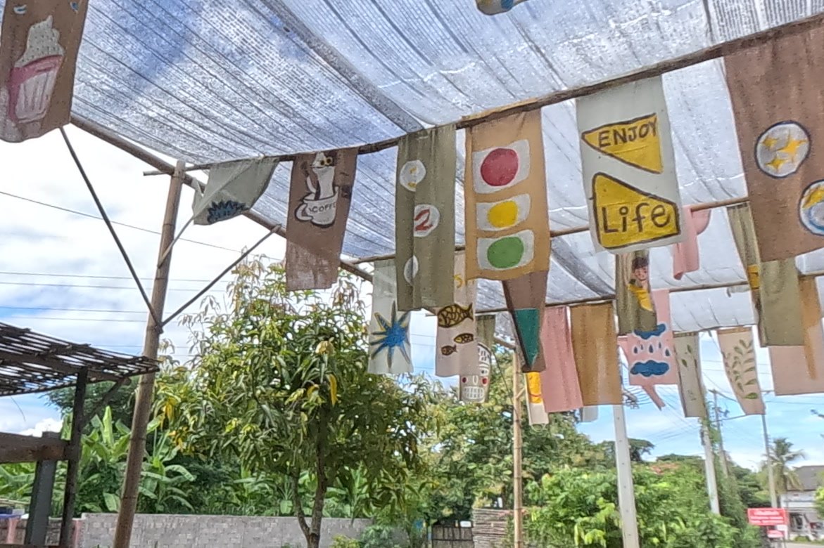 Painted cloth flags over the lane — Chamcha Market, San Kamphaeng