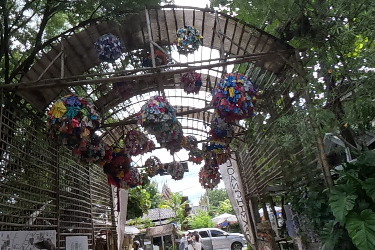 Fabric pom-poms hanging over the lattice arch — Chamcha Market, San Kamphaeng