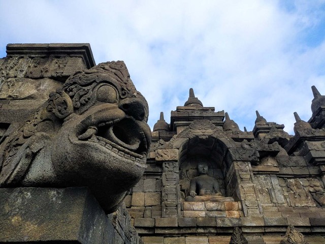 A stone makara water spout (jaladwara) projecting from the wall of Borobudur in Java, with a seated Buddha in a niche behind it.