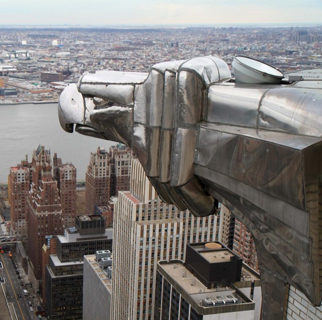 A stainless-steel eagle head projecting from a corner of the Chrysler Building in New York, with the city far below.